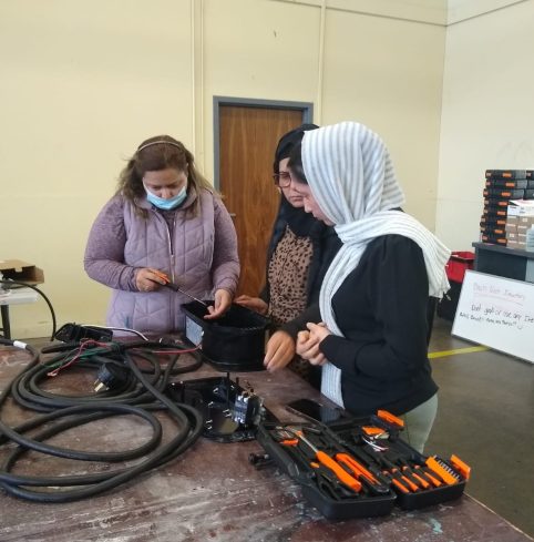 Three participants in a hands-on electrical training workshop, working with cables and tools at a bench